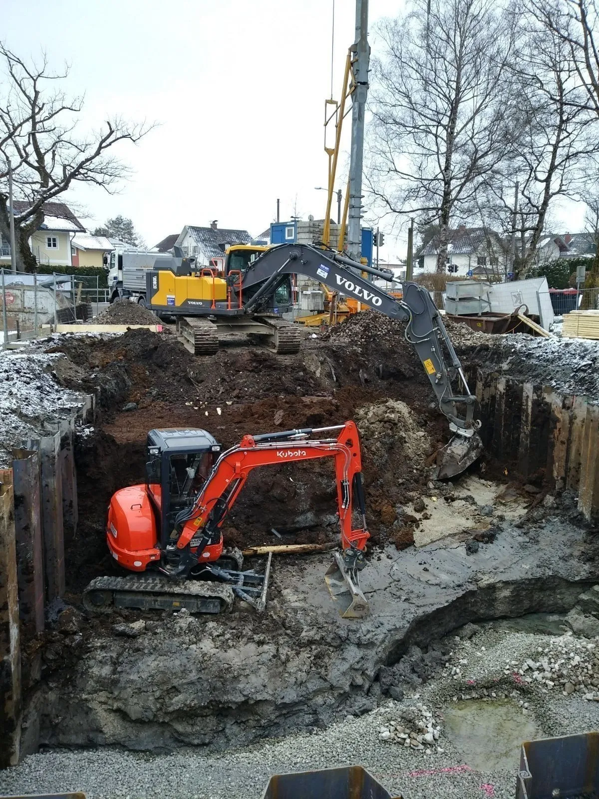 Große Baugrube mit Spundwänden, Bagger oben an der Kante und unten in der Grube