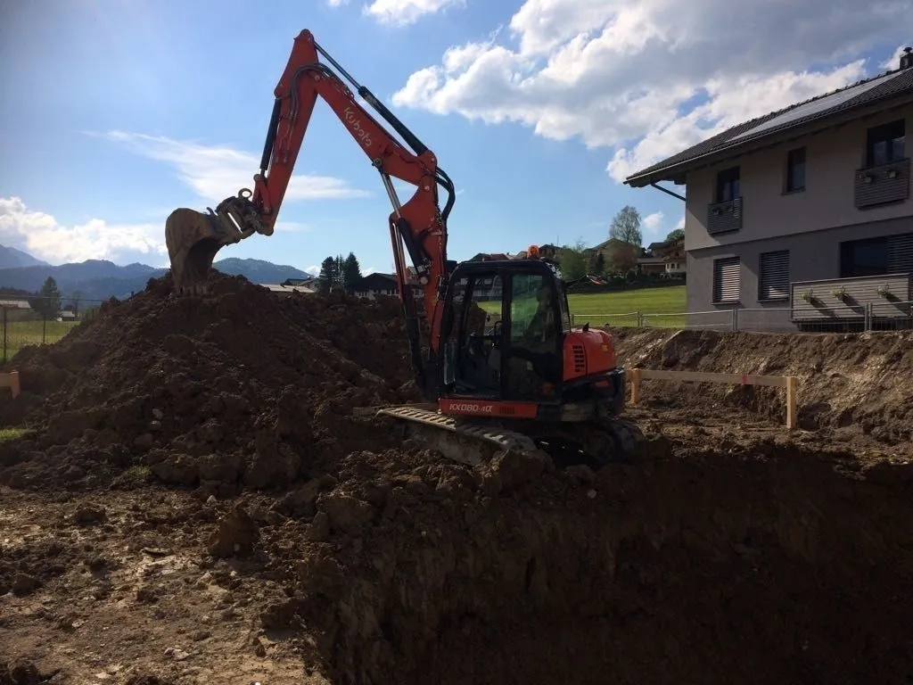 Kubota-Bagger beim Baugrubenaushub neben einem Wohnhaus