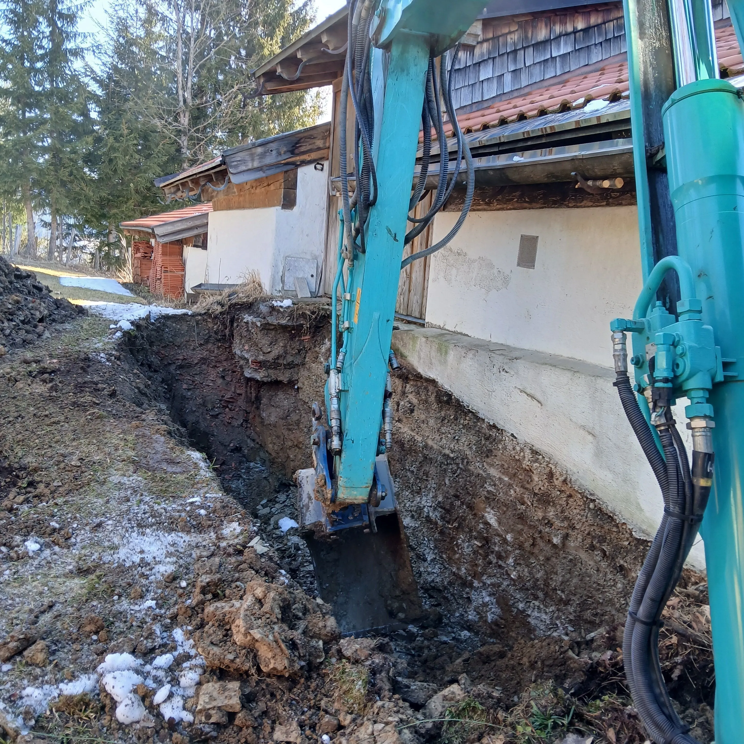 Baggerlöffel hebt einen schmalen Graben entlang einer Hausmauer aus