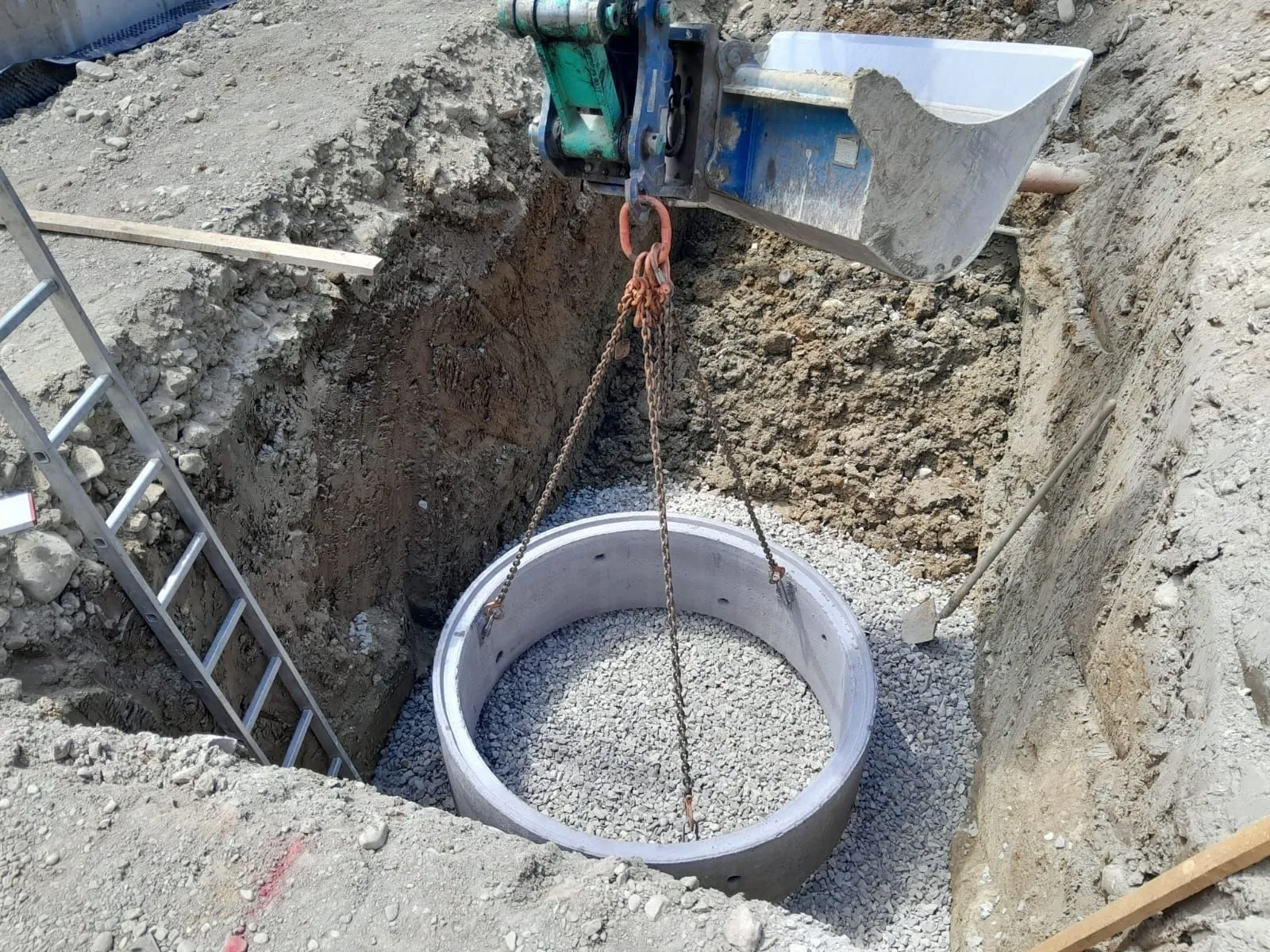 Bagger setzt einen Betonschachtring in eine ausgehobene Baugrube