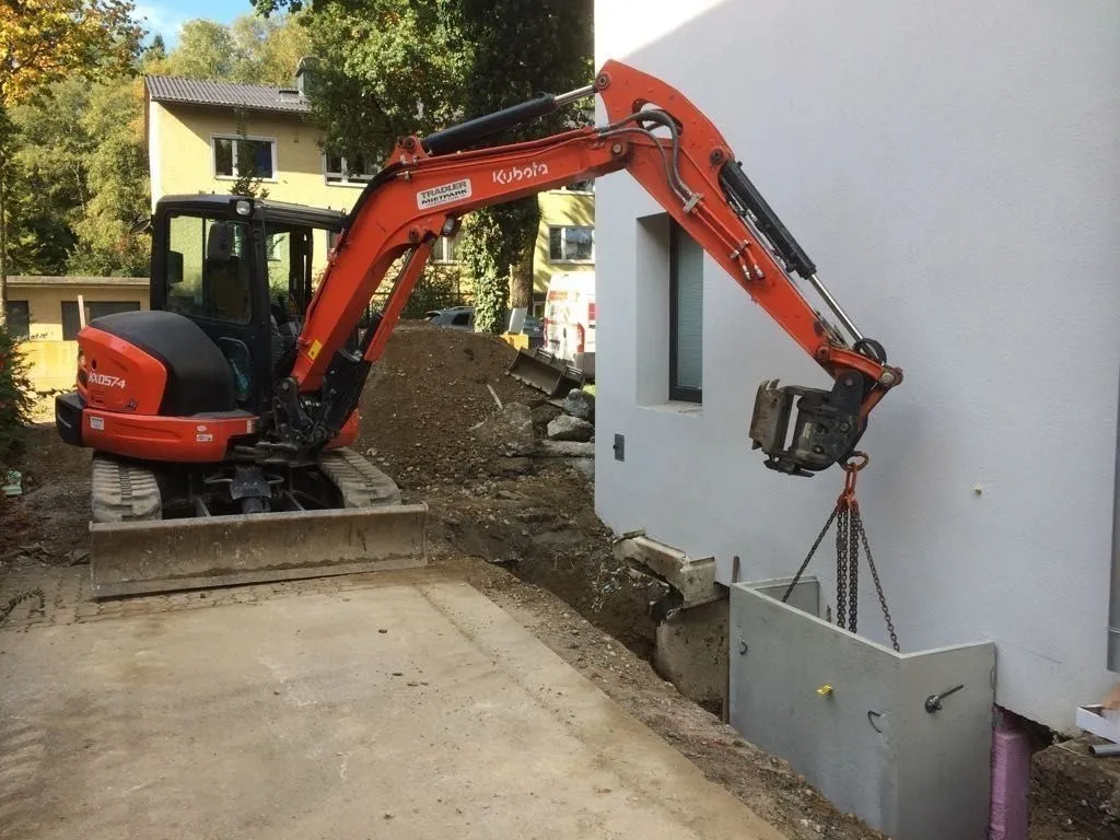 Bagger versetzt ein Betonfertigteil an einer Hausfassade