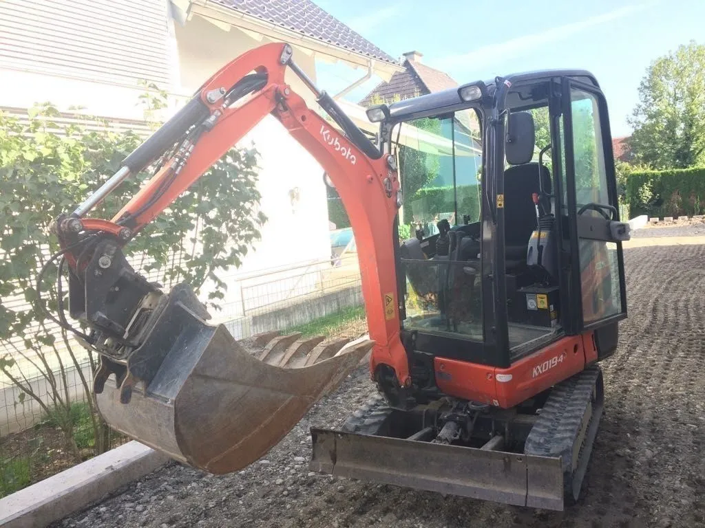 Minibagger mit erhobenem Arm auf frisch planierter Schotterfläche
