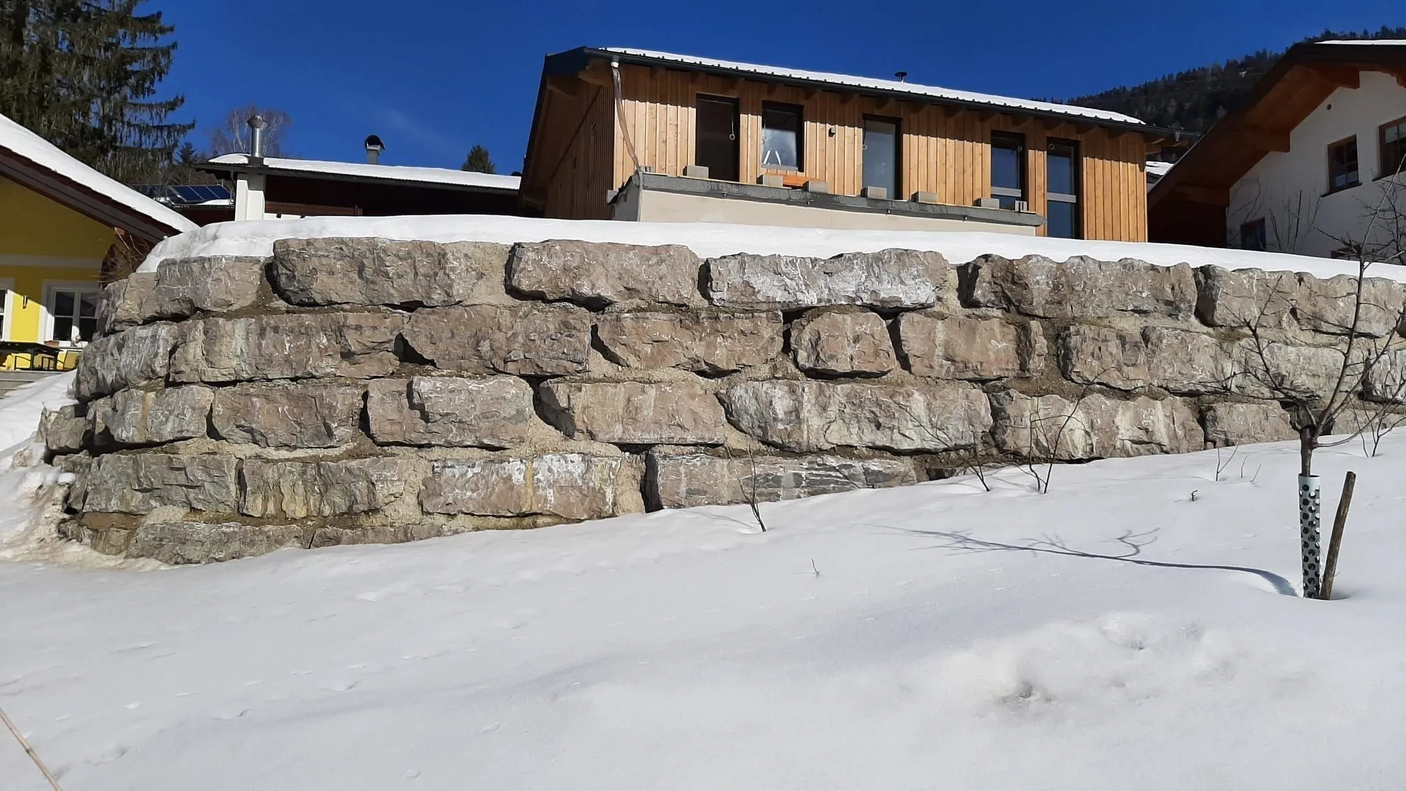 Mehrlagige Natursteinmauer als Hangabfangung vor einem Wohnhaus, schneebedeckt