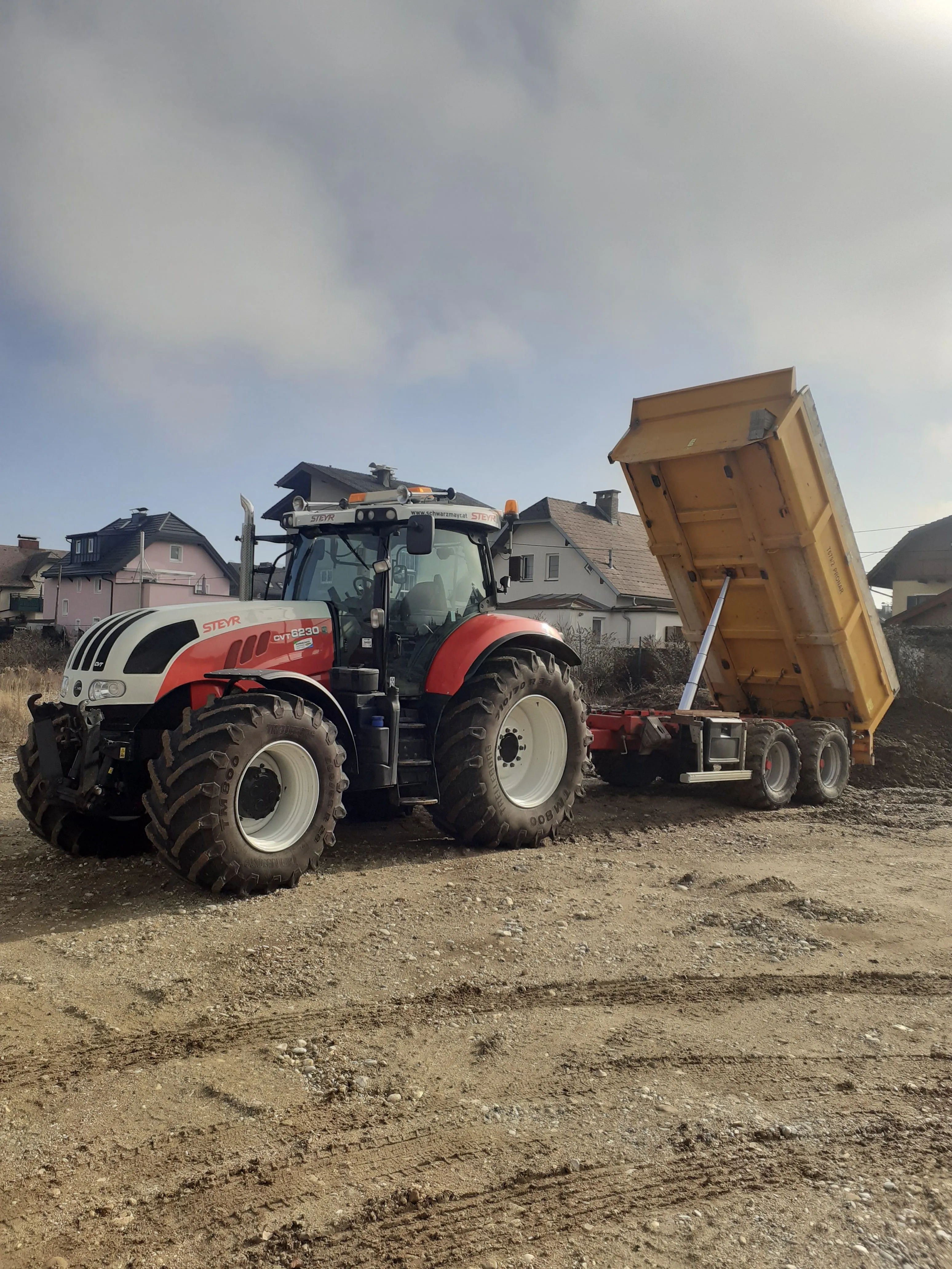 Traktor mit hochgekipptem Muldenanhänger beim Abladen von Schüttgut