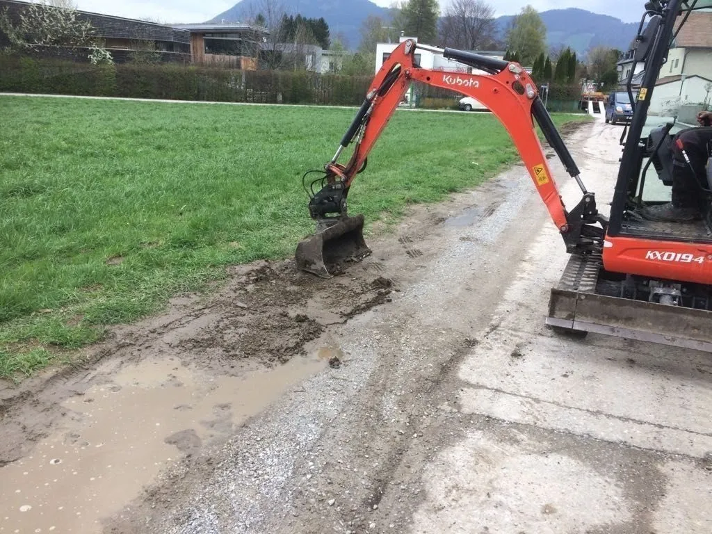Minibagger zieht das Bankett entlang eines Schotterwegs ab
